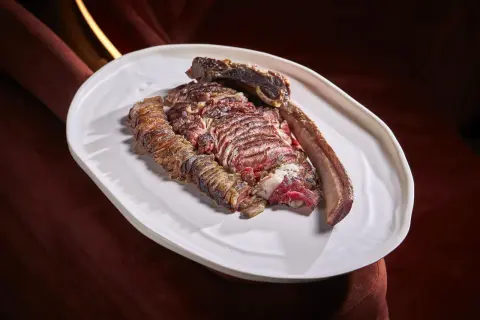 A perfectly cooked chuleton, a thick-cut bone-in steak, rests on a white platter, showcasing its juicy, red interior and seared crust.