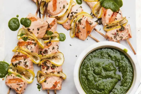 Grilled salmon skewers with lemon slices and a vibrant green sauce, ready to be dipped.