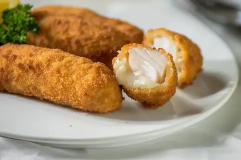 Golden cod croquettes, one split open to reveal flaky white fish and creamy filling, served on a white plate with a sprig of parsley.
