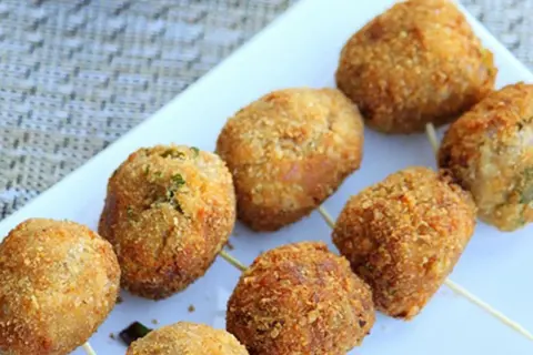 Golden-brown tuna balls on skewers, coated in crispy breadcrumbs, are arranged on a white platter.