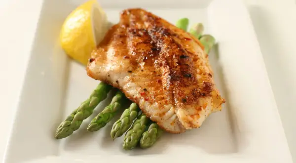A perfectly seasoned fish fillet rests on a bed of asparagus, a lemon wedge on the side. A delightful dish inspired by Spanish fish recipes.