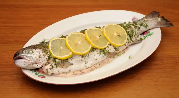 A whole trout, seasoned and garnished with lemon slices and herbs, ready to be cooked as trucha a la navarra.