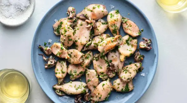 A plate of tender baby squid food, seasoned with herbs and served with a side of salt and white wine.
