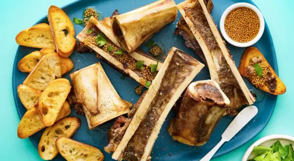 Roasted bone marrow halves served with toasted baguette slices, whole grain mustard, and parsley. A delicious bone marrow recipe.