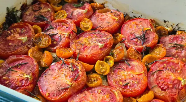 A baking dish filled with juicy, slow roasted tomatoes and cherry tomatoes, seasoned with herbs and spices.
