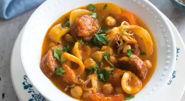 A hearty Spanish stew with tender squid rings, chickpeas, and chorizo in a rich tomato sauce, garnished with fresh parsley.