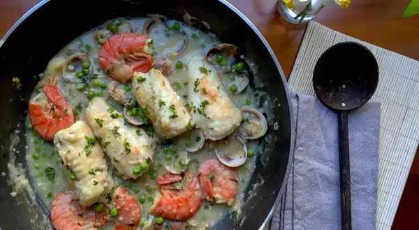 A delicious bonito fish recipe with prawns, clams, and peas in a creamy sauce, garnished with parsley.