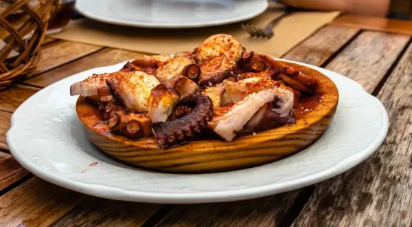 A delicious Spanish octopus dish, seasoned with paprika and served on a wooden platter on a rustic table.