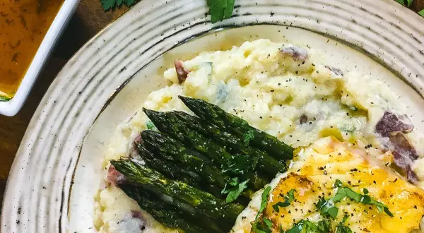 A delicious grouper recipe featuring pan-seared fish, creamy mashed potatoes with red skin, and roasted asparagus, all garnished with fresh parsley.