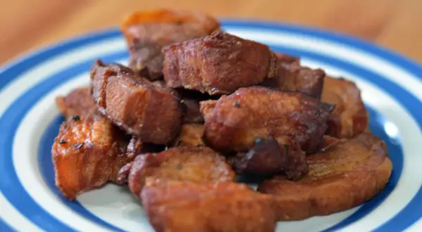 A pile of crispy fried pork belly, or chicharrones, on a blue and white striped plate.