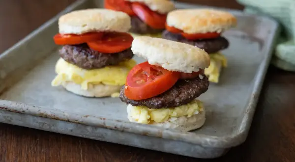Fluffy biscuits layered with scrambled eggs, a savory goose sausage patty, and fresh tomato slices.