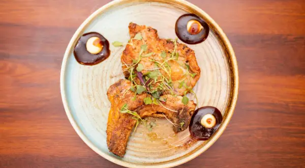Two pieces of grilled steak, garnished with microgreens, are served as steak tapas with a rich sauce and a dollop of cream.