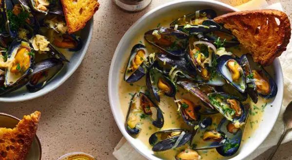 A delicious bowl of moules marinière, brimming with plump mussels in a creamy broth, served with crusty bread and a glass of beer.