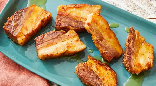 Crispy pork belly, Spanish style, glistening on a teal platter with a hint of green oil.