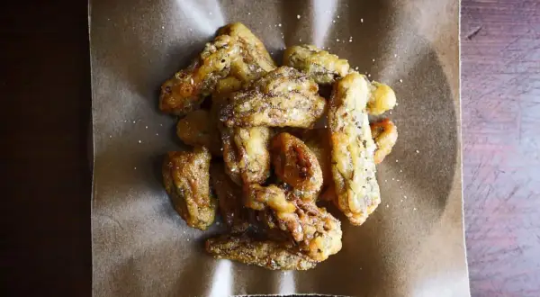 Crispy, golden fried morel mushrooms, lightly salted, piled on brown parchment paper. A delicious appetizer.