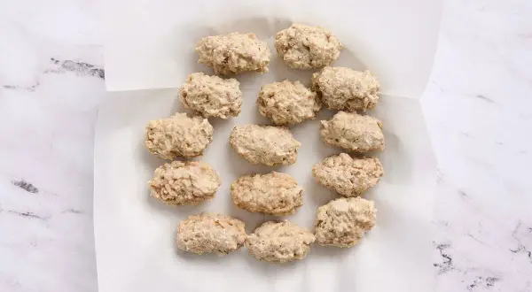 A dozen uncooked croquetas de pollo are arranged on white parchment paper, ready for frying.