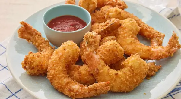 Crispy fried shrimp piled high on a plate, with a small bowl of red dipping sauce.