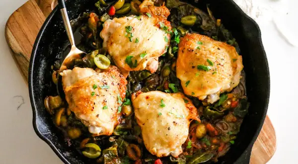 Four golden chicken thighs nestled in a rich, rustic chicken basque stew with olives and peppers, garnished with fresh parsley.