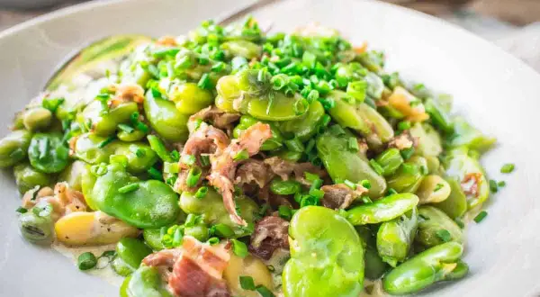 A delicious dish showing how to cook fava beans with bacon and chives, served in a creamy sauce on a white plate.