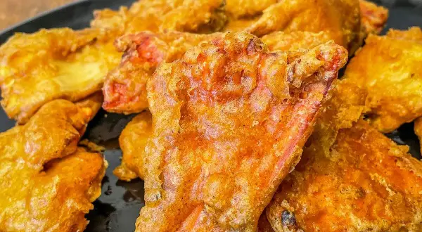 Crispy, golden-fried pieces, possibly part of a delicious chicken of the woods recipe, piled on a black plate.
