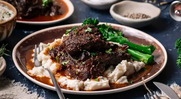 Tender beef cheek, Spanish style, served with creamy mashed potatoes and vibrant green vegetables.