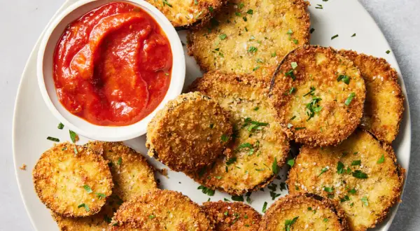 Crispy spanish fried eggplant slices, golden brown and seasoned, served with a side of vibrant tomato sauce and sprinkled with fresh parsley.