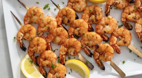 A platter of perfectly grilled shrimp skewers, seasoned and garnished with fresh parsley and lemon wedges.