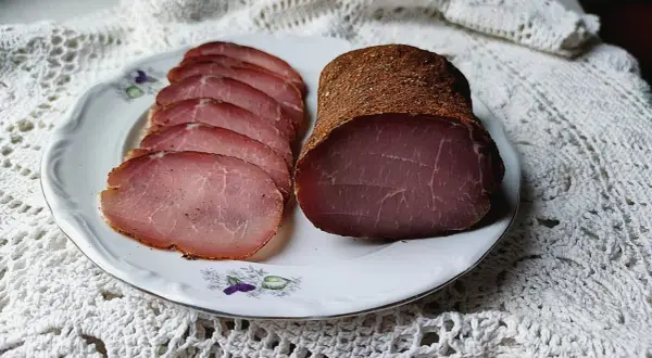 A whole and sliced cured pork loin, seasoned with spices, rests on a decorative plate.