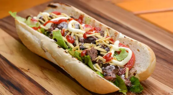 A delicious pepito sandwich overflowing with tender steak, crisp lettuce, tomato, shoestring fries, and drizzled with ketchup and mayonnaise.