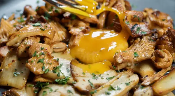 A fork breaks a rich egg yolk over a bed of perfectly grilled mushroom recipe, garnished with fresh parsley.