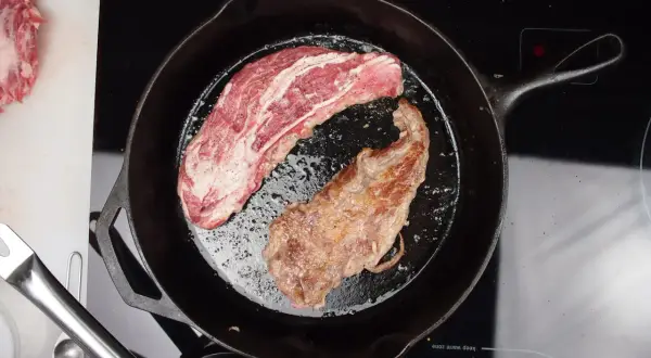 A pluma steak, a prized cut from the pork loin, sizzles in a cast-iron skillet. One side is perfectly seared, the other still raw and marbled.