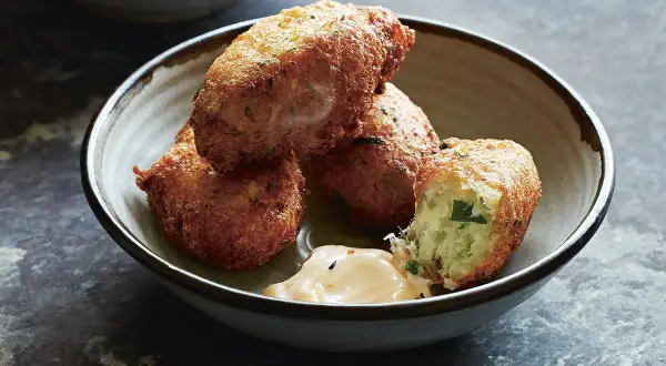 Golden-brown croquetas de bacalao, one broken open to reveal a fluffy interior, sit in a rustic bowl with a dollop of creamy sauce.