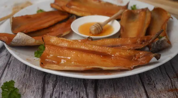 A plate of glistening smoked trout fillets, with a small dish of honey and a honey dipper. A delicious start to any meal.