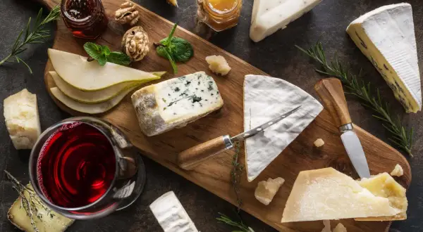 A beautiful spread of wine and cheese pairings, featuring a glass of red wine, various cheeses, pears, walnuts, and honey on a wooden board.