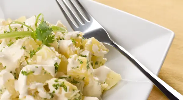 A delicious ensalada rusa española, featuring creamy potato salad with fresh herbs and a fork ready to dig in.