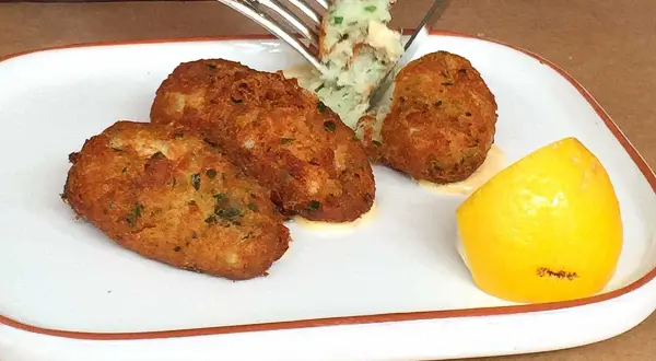 Golden brown cod fritters served with a dollop of mashed potatoes and a lemon wedge. A fork is lifting a bite of the fritter.