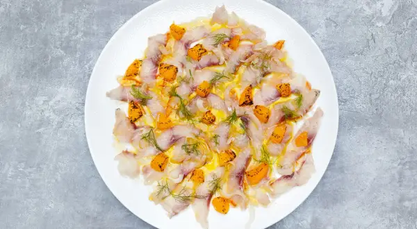 Thinly sliced sea bass crudo, glistening with olive oil and dotted with bright orange citrus segments and fresh dill.