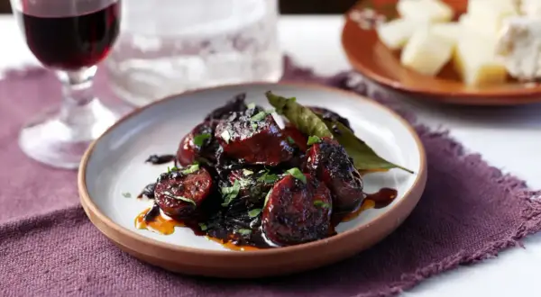 Delicious chorizo tapas, glazed and garnished with parsley, served with a glass of red wine and cheese.