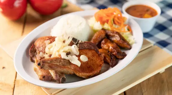 A delicious plate of chuleta meat, a flavorful pork chop, served with rice, fried plantains, salad, and beans.