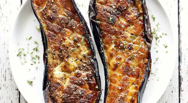 Two halves of baked eggplant, seasoned and sprinkled with herbs, are a delicious start to many eggplant recipes.