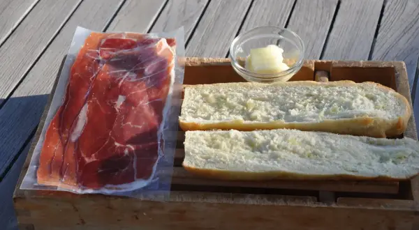 Ingredients for a delicious jamon iberico sandwich: thinly sliced cured ham, buttered bread rolls, and a small dish of butter.