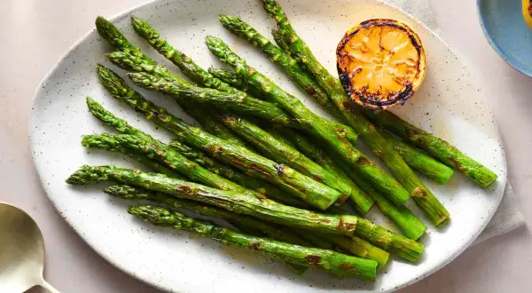 A plate of perfectly grilled spanish asparagus, lightly charred and served with a grilled lemon slice.