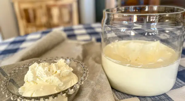 A small glass bowl overflows with fluffy crème fraîche, next to a jar of the creamy dairy product.