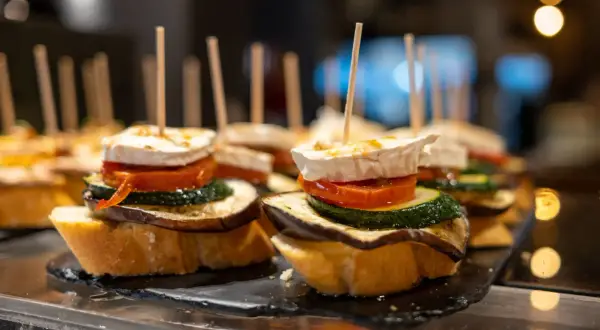 A delicious charcuterie board featuring stacked tapas on toasted bread, topped with goat cheese, tomato, zucchini, and eggplant.