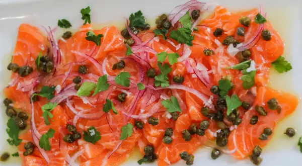 Thinly sliced salmon crudo, dressed with olive oil, capers, red onion, and parsley, is a refreshing appetizer.