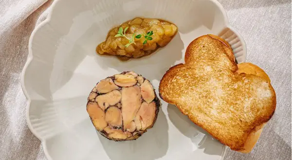 A slice of duck terrine with a dollop of compote and heart-shaped toast on a scalloped plate.