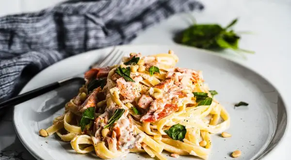 A plate of creamy smoked salmon pasta, garnished with fresh basil and pine nuts.
