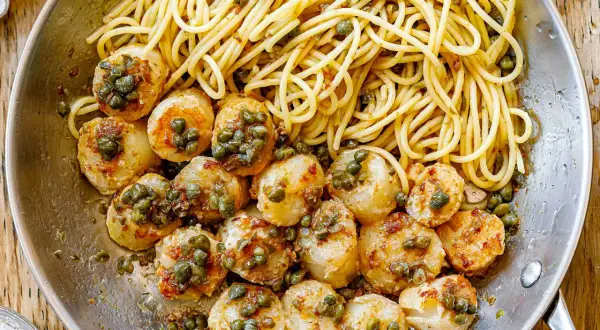 A delicious scallops and pasta recipe with white wine sauce, garnished with capers, served in a skillet.