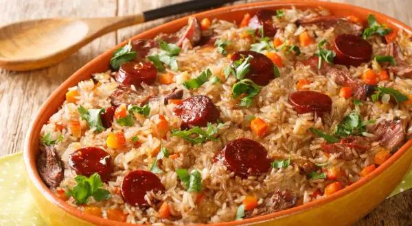A hearty dish of rice with sauteed chorizo, tender meat, and diced carrots, garnished with fresh parsley.