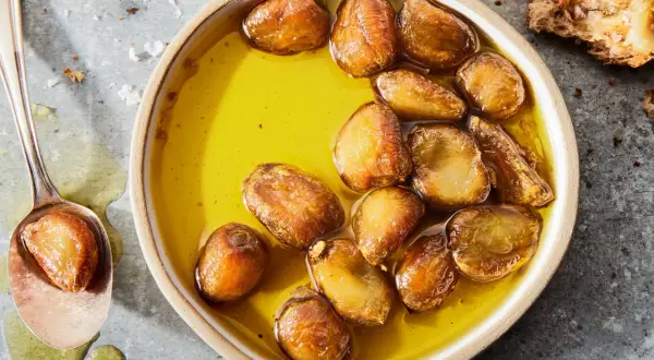 Golden garlic cloves swimming in olive oil, a delicious result of how to make garlic confit. A spoon holds one tender clove.